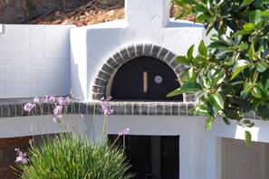 A white building with a black arched entrance and a thermometer on the wall. - Elounda Villa Kalydon (Plaka)