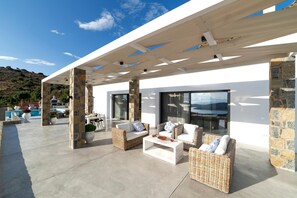 A modern outdoor patio with stone pillars, wicker furniture, and a pool. - Elounda Villa Kalydon (Plaka)