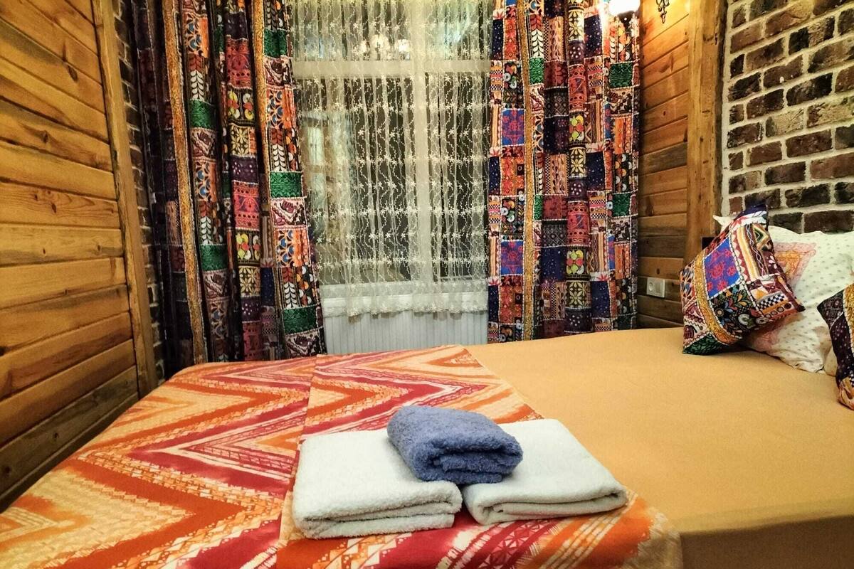 Ein Zimmer mit einem Bett, gemusterten Vorhängen und einem Fenster mit Spitzengardinen.