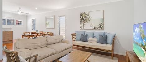 A living room with a sofa, chairs, a coffee table, a TV, and a dining area with a table and chairs.