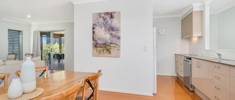 Ett modernt kök med diskmaskin, en matplats med ett träbord och stolar samt en stor tavla på väggen.