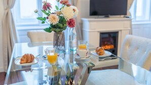 Una mesa de desayuno con cruasanes, zumo de naranja y un jarrón de flores.