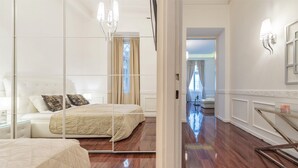 Una habitación de hotel con un espejo grande, una cama con cubrecama color beige, una mesita de noche y un atril.