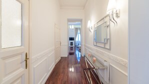 Un pasillo con piso de madera pulida, paredes blancas y un espejo con luces empotradas.