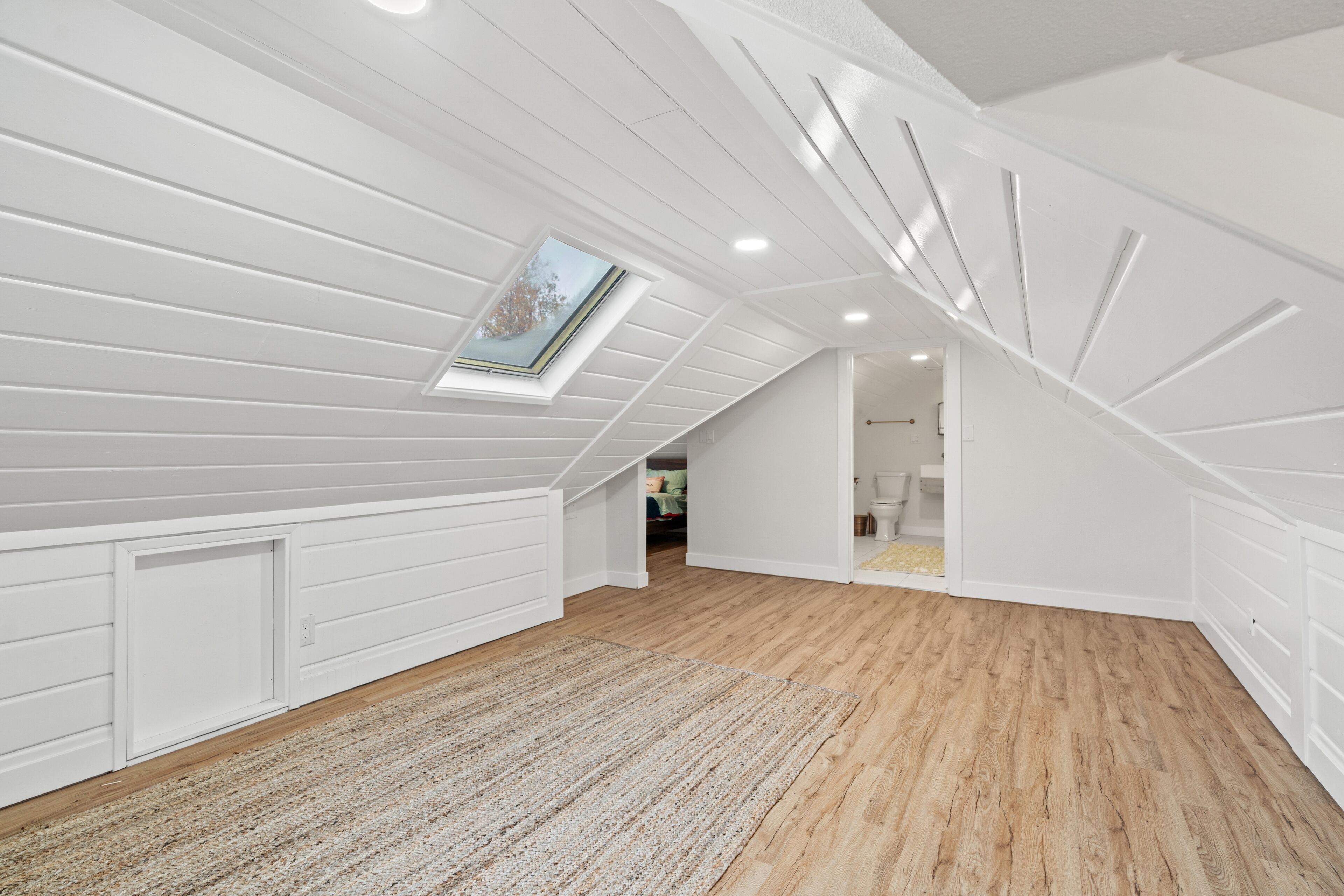 A spacious attic room with wooden flooring, white walls, and a skylight.