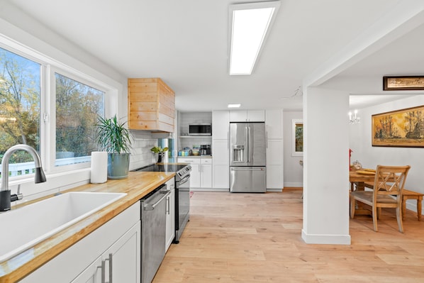 A modern kitchen with a large window, stainless steel appliances, and a wooden dining table.