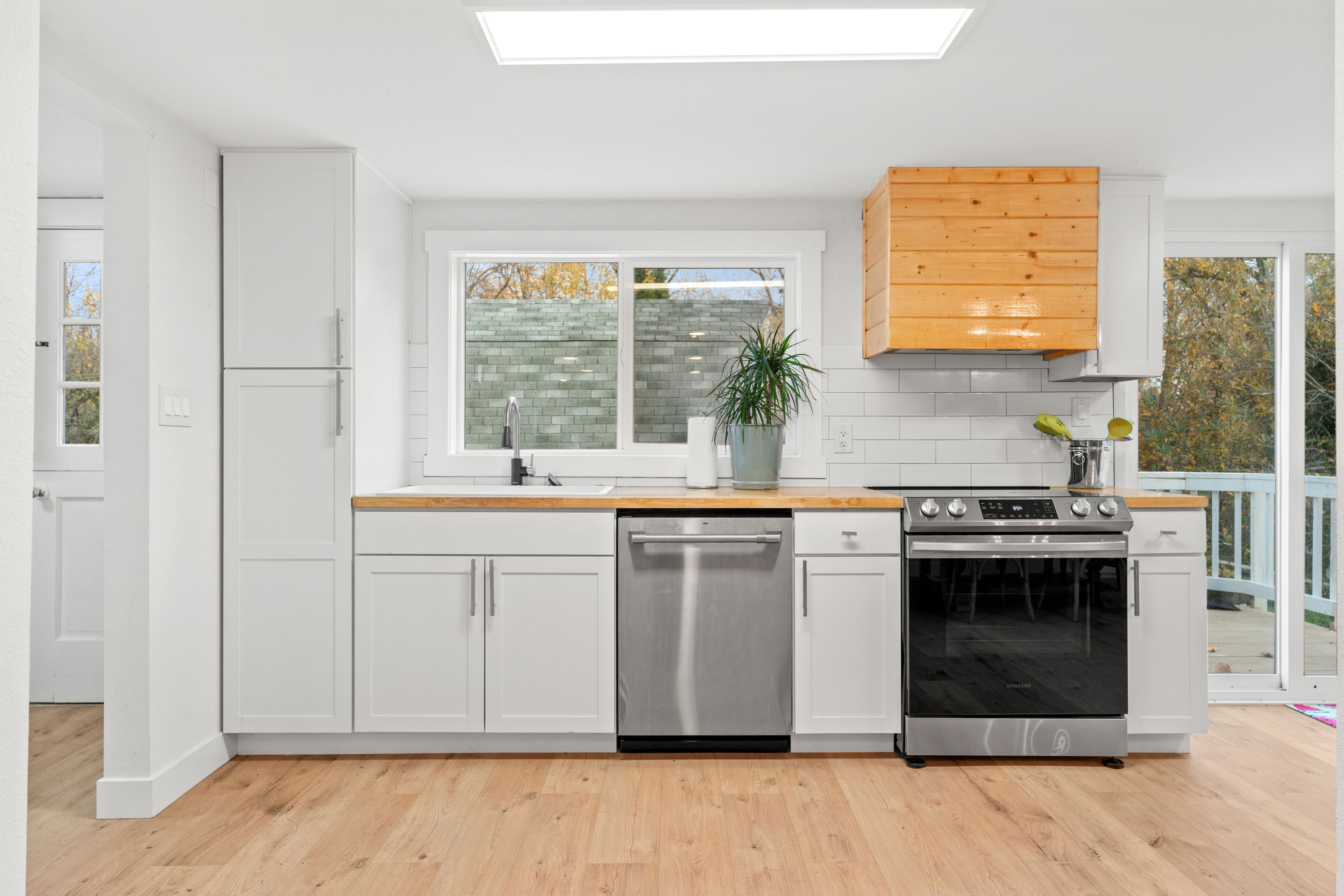 Una cucina moderna con mobili bianchi, una lavastoviglie in acciaio inossidabile, un forno e un pensile in legno.
