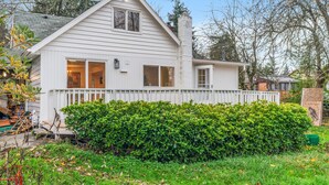 Une maison blanche à deux étages, dotée d’un porche à l’avant, d’une cheminée et d’une haie bien entretenue dans le jardin.