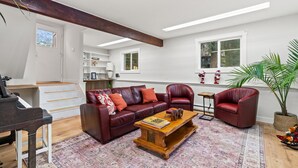 Un salon spacieux avec un piano, un canapé en cuir rouge, une table basse en bois et une grande fenêtre laissant entrer la lumière naturelle.