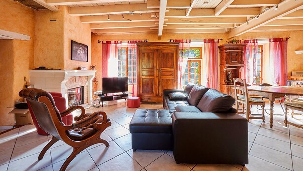 Ein gemütliches Wohnzimmer mit Kamin, Ledersofa, Holzschrank und einem Essbereich mit Tisch und Stühlen.