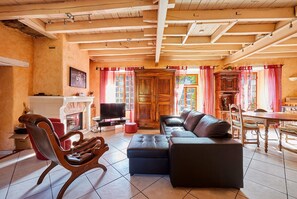 A cozy living room with a fireplace, leather sofa, wooden cabinet, and a dining area with a table and chairs. - MOULIN Menhirs & nature reserve (Saint-Just)