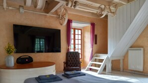Ein Schlafzimmer mit Bett, Sessel, Schreibtisch, Fernseher und einem Fenster mit Vorhängen.