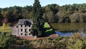 Ein Steinhaus mit einem geneigten Dach, einem Balkon und einem Teich im Vordergrund.