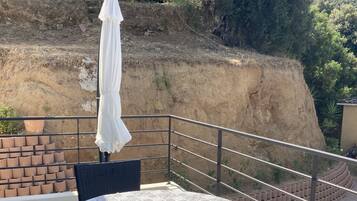 A balcony with a round table and chairs, a white umbrella, and a view of a hillside.