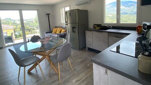 Una cocina moderna con refrigerador integrado, un área de comedor con mesa y sillas de vidrio, y vistas a un paisaje montañoso a través de amplios ventanales.