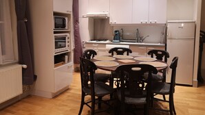 Une cuisine compacte avec des meubles blancs, une table à manger avec quatre chaises, un four à micro-ondes, un grille-pain et une machine à café.