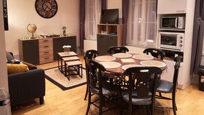 Un espace de vie compact comprenant une table à manger entourée de chaises, un canapé, un téléviseur et une kitchenette équipée d’un four à micro-ondes.