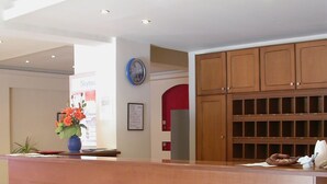 A reception desk with a wooden finish, a clock on the wall, and a framed poster. - Kassandra Bay (Kassandra)