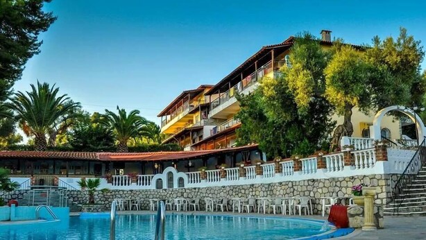 A hotel with a swimming pool, outdoor seating, and a multi-story building with balconies. - Kassandra Bay (Kassandra)