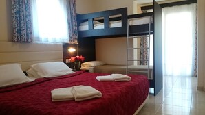 A hotel room with a bunk bed, a red bedspread, white pillows, a bedside table with a lamp, and a vase with flowers. - Kassandra Bay (Kassandra)