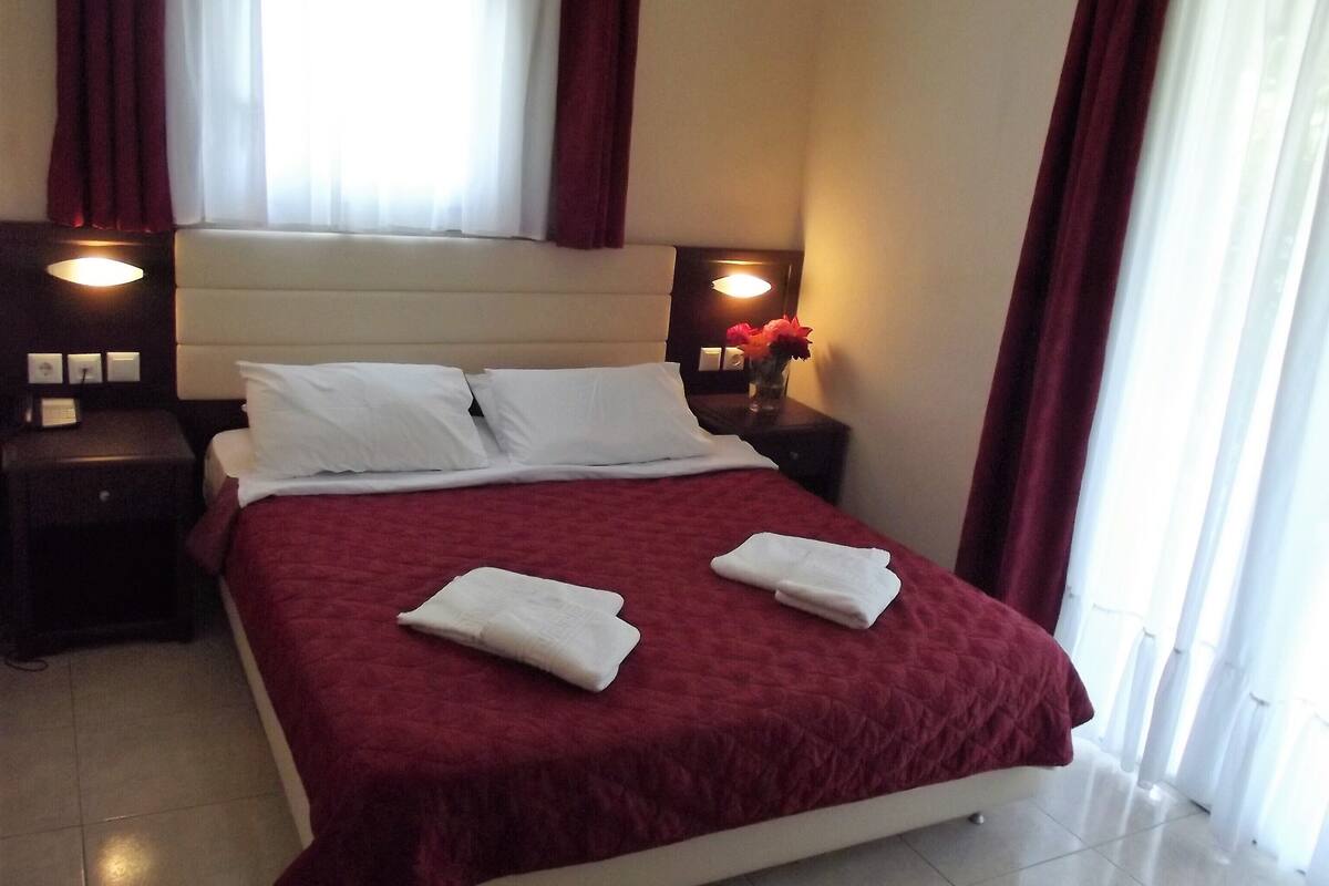 A neatly made bed with a red bedspread and white pillows, two bedside tables with lamps, and a vase with flowers on one of the tables.