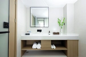 A modern bathroom with a white sink, a mirror, and a wooden shelf with towels.