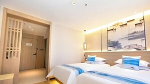 A hotel room with two beds, a wooden door, a wall-mounted artwork, and a ceiling light. - JiHe Hotel (Jiaozuo Railway Station Puji Road) (Jiaozuo)