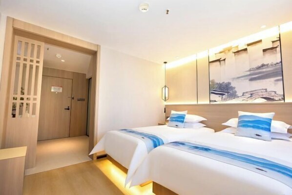 A hotel room with two beds, a wooden door, a wall-mounted artwork, and a ceiling light. - JiHe Hotel (Jiaozuo Railway Station Puji Road) (Jiaozuo)