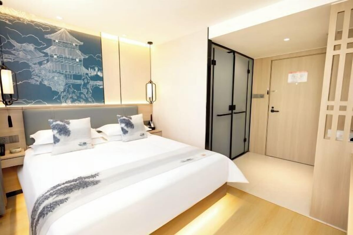 A modern hotel room with a large bed, a nightstand, a wall-mounted lamp, and a sliding door closet.