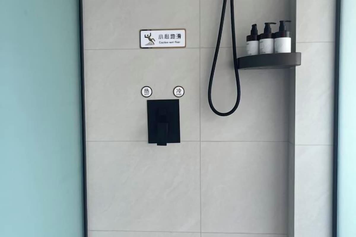 A bathroom with a towel rack, a shower control panel, and a shelf with toiletries.