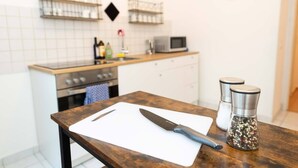 A kitchen with a wooden table, a cutting board, a knife, salt and pepper shakers, a microwave, and a stove.
