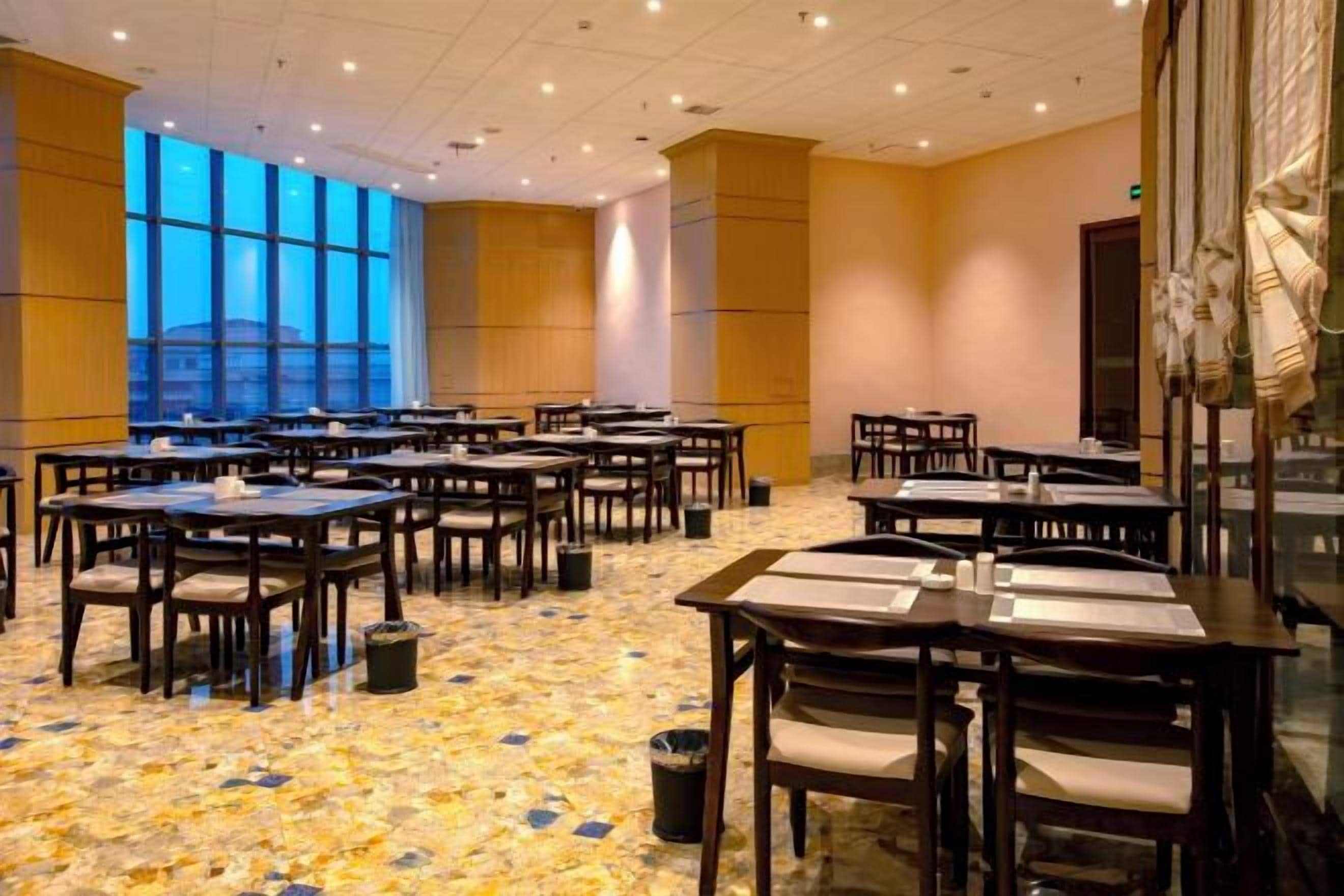 A conference room with multiple tables and chairs, large windows, and a carpeted floor.