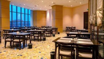 A conference room with multiple tables and chairs, large windows, and a carpeted floor.