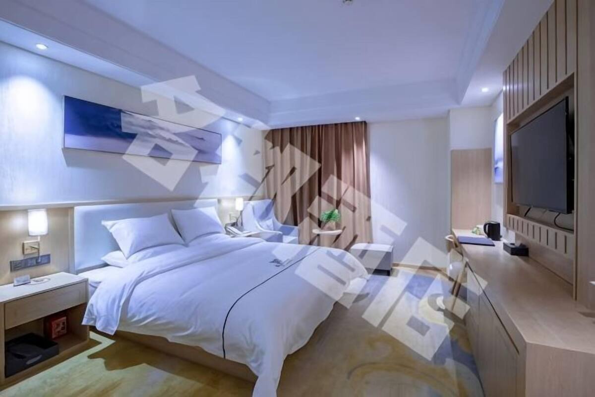 A modern hotel room with a bed, bedside tables, a TV, and a large window.