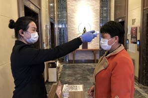 A person wearing a mask and gloves conducting a temperature check on another individual. - Mingdu Hotel (Wuyang)