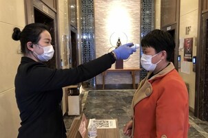 Una persona con mascarilla y guantes toma la temperatura a otra persona.