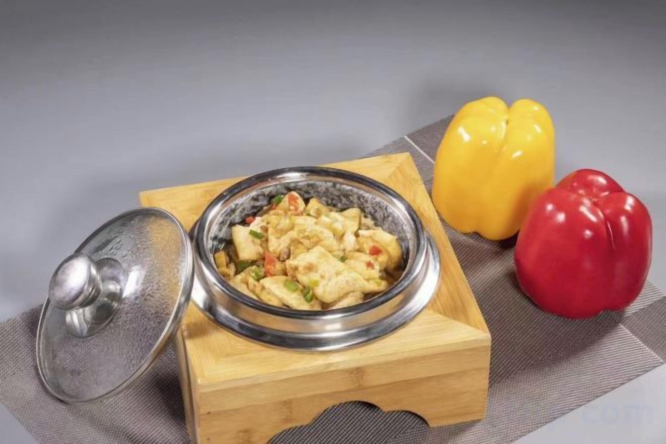 Un plato de comida sobre un bloque de madera con tapa, acompañado de dos pimientos.