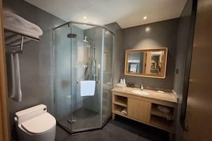 Un baño moderno con ducha envuelta en vidrio, inodoro, tocador con espejo y perchero.
