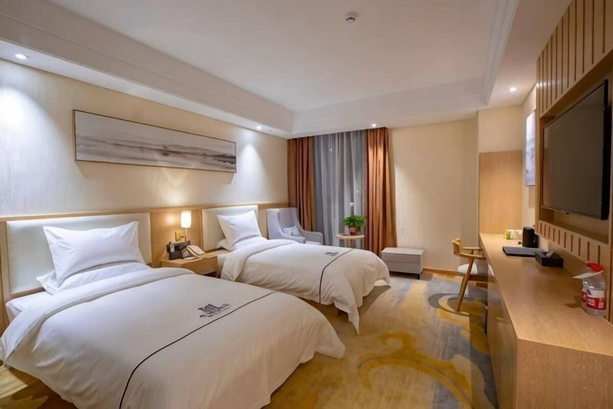 A hotel room with two beds, a desk, a TV, and a large window with curtains.
