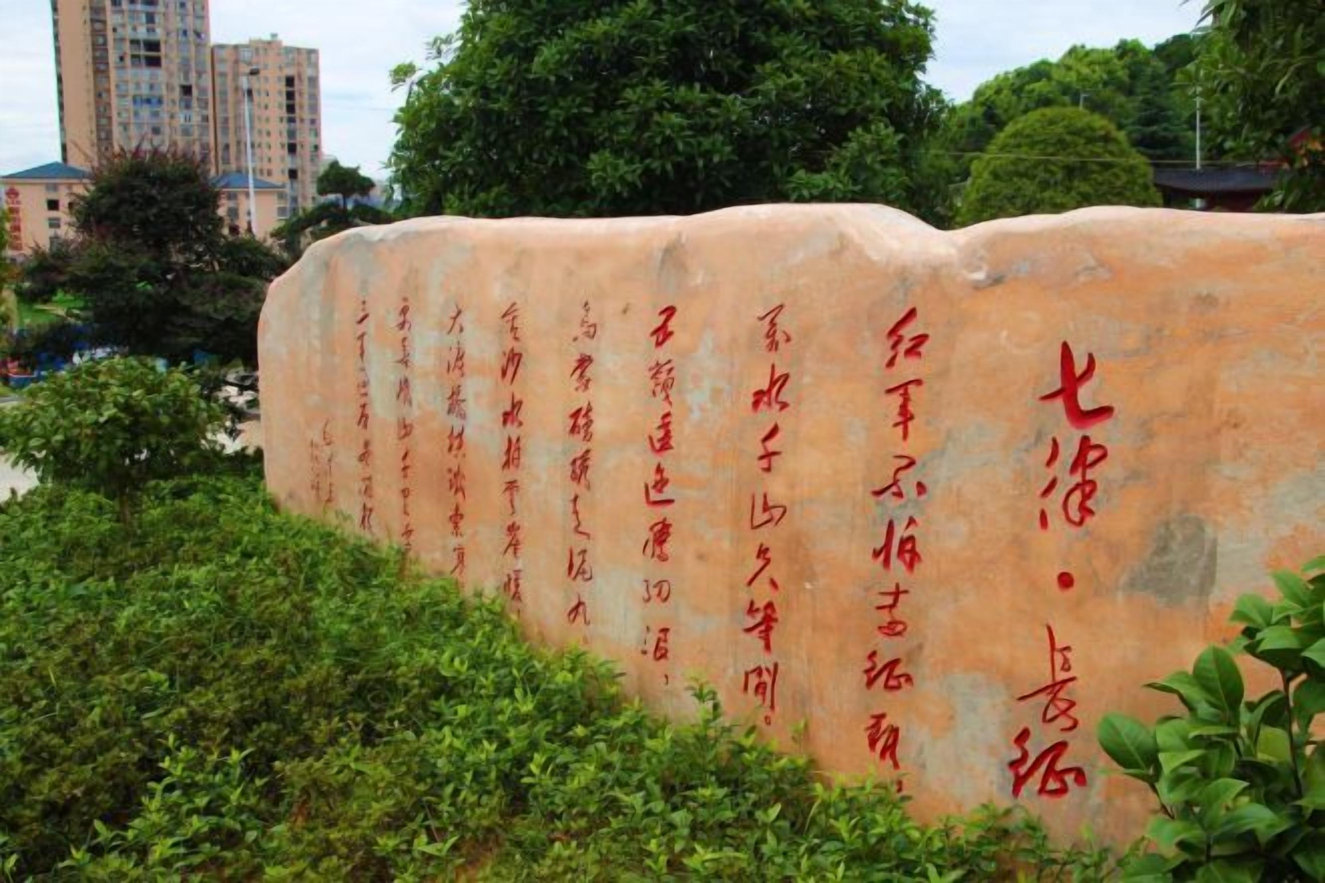 A stone monument with inscriptions, surrounded by greenery.
