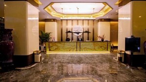 A reception area with a marble floor, a reception desk with two staff members, a large decorative globe, and a television on the right. - Mingdu Hotel (Wuyang)