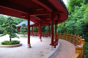 Um pavilhão coberto com telhado curvo, cercado por uma vedação de madeira e vegetação.