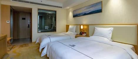 A hotel room with two beds, a large window, a painting on the wall, and a small table with a lamp.