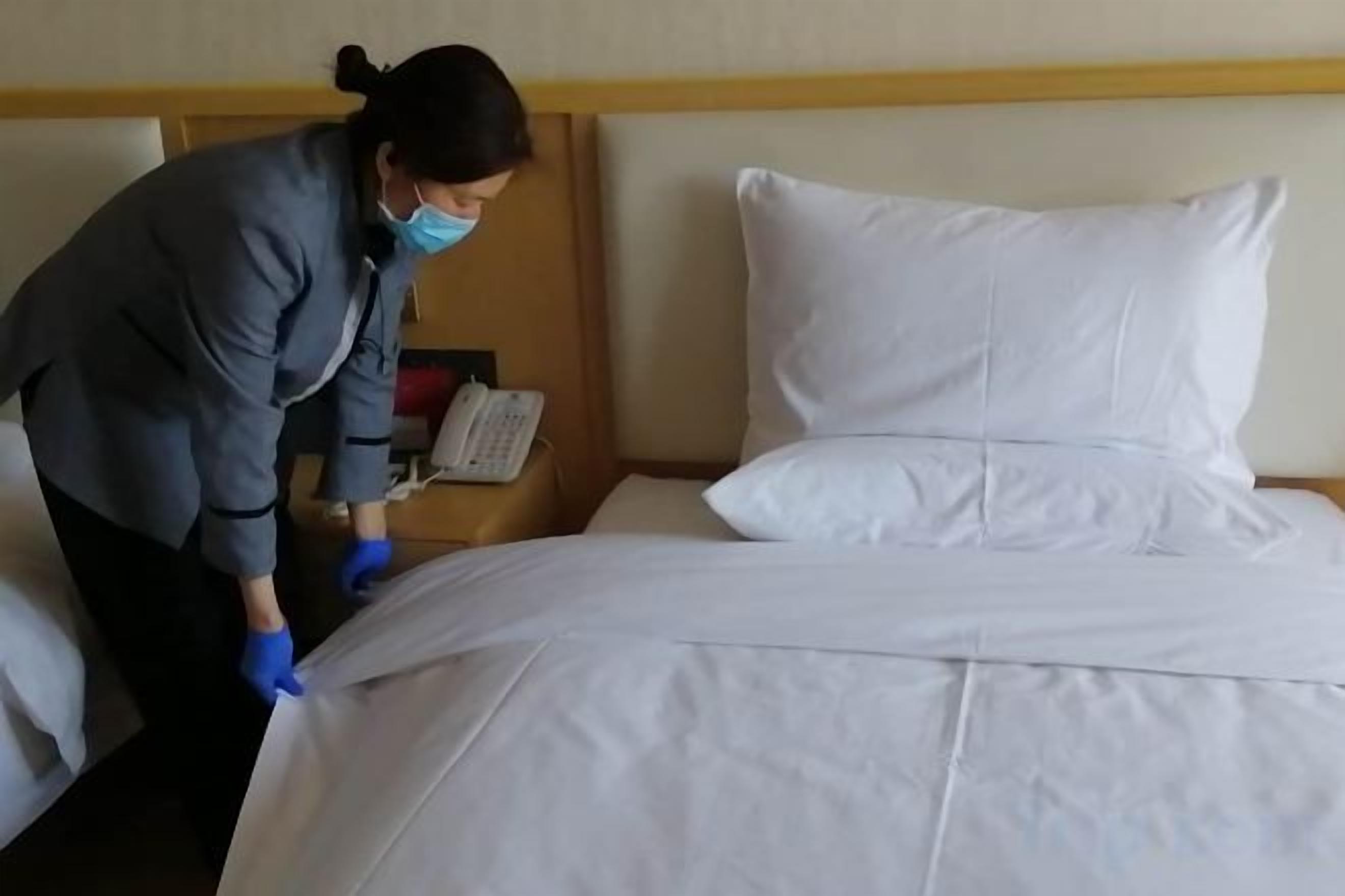Una persona limpiando una cama en una habitación de hotel.
