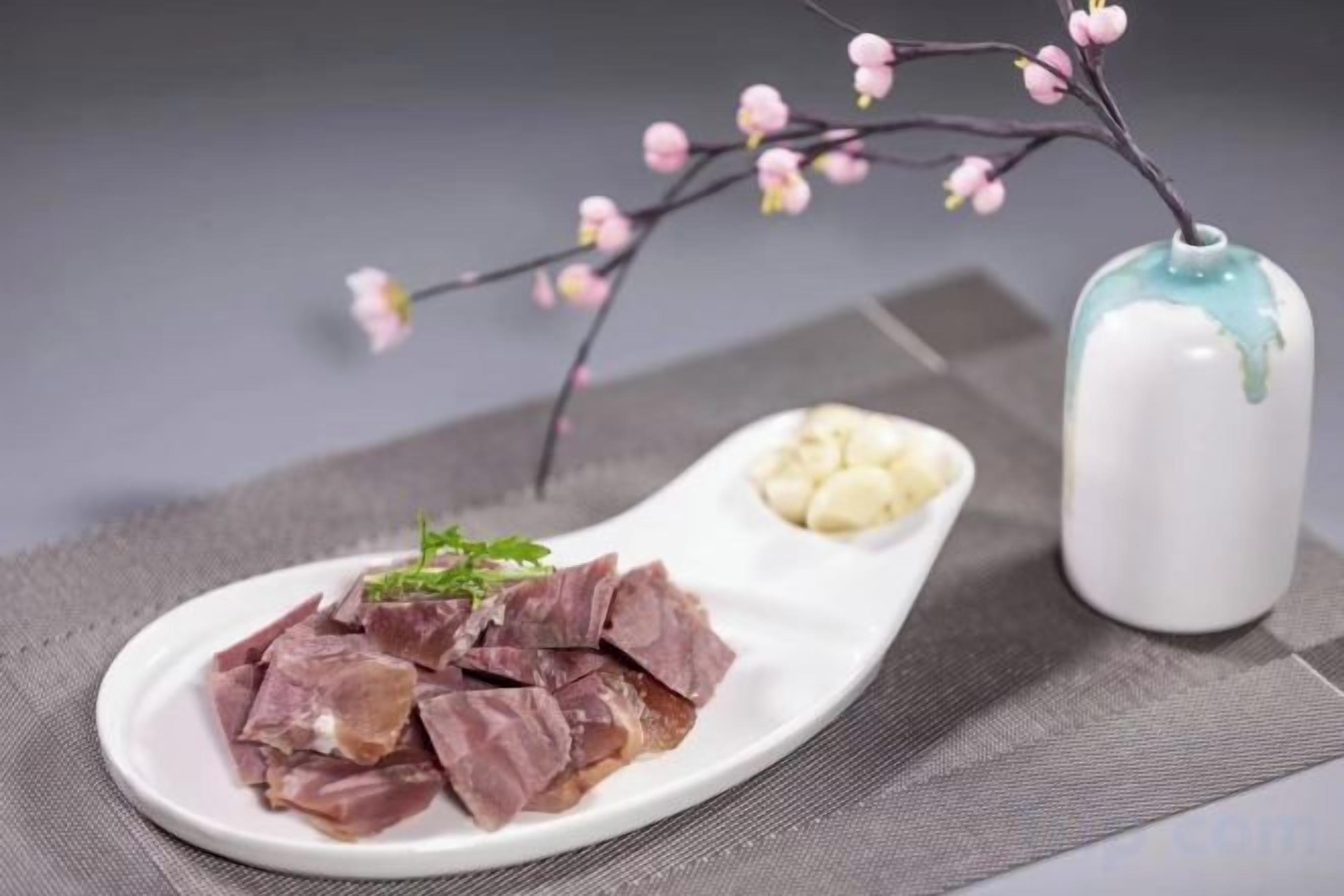 Un plato blanco con alimentos y un pequeño jarrón con una rama.