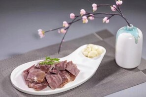 A white plate with food items and a small vase with a branch. - Mingdu Hotel (Wuyang)