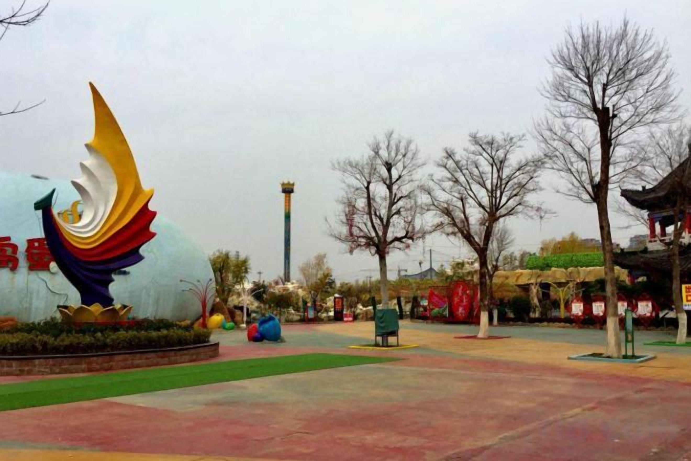 A public square with a large decorative sculpture, a green lawn, and bare trees.