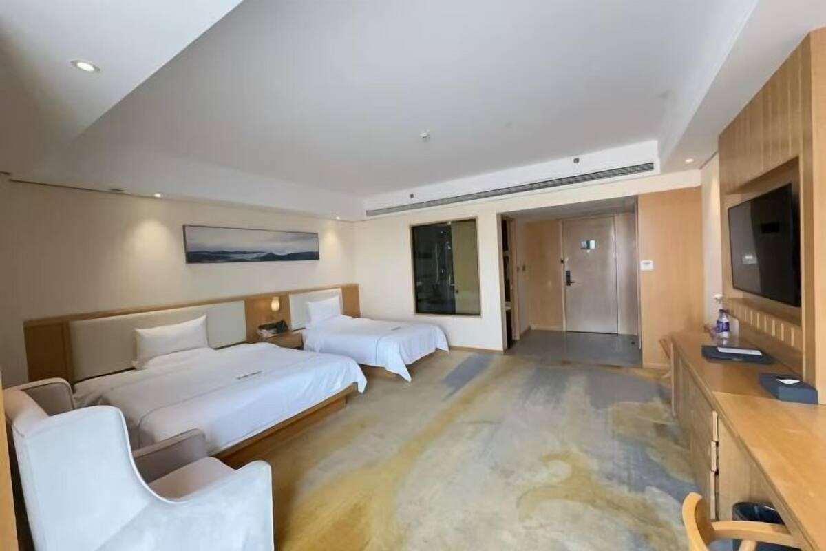 A hotel room with two beds, a desk, a chair, a TV, and a painting on the wall.
