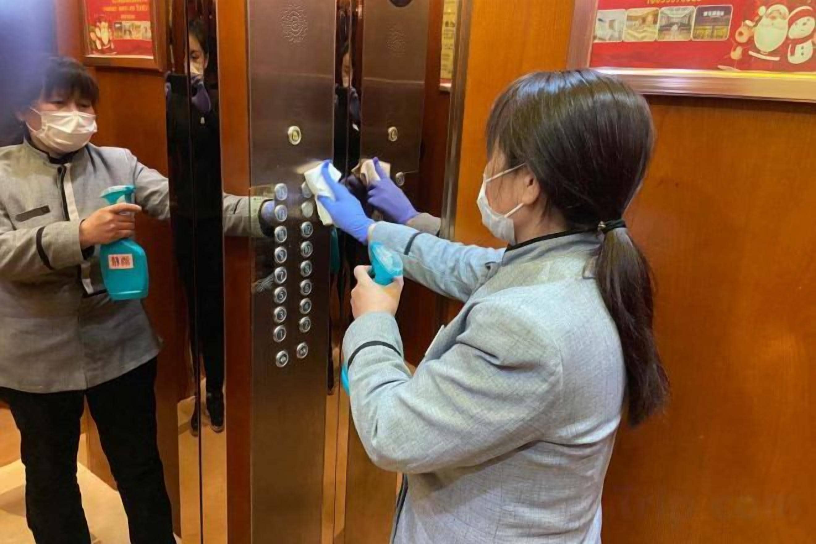 Two individuals cleaning an elevator door with spray bottles.
