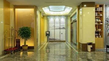 A hotel lobby with a marble floor, a reception desk, a plant, and a bookshelf.